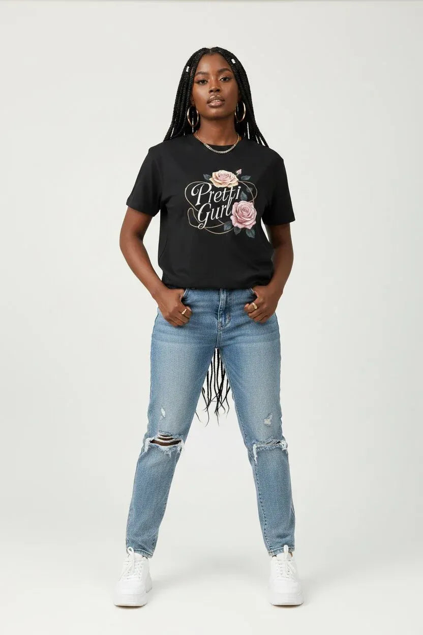 A woman modeling a black graphic t-shirt with 'Pretend Girl' and a rose design, paired with light-wash distressed jeans and white sneakers, against a plain light gray background.