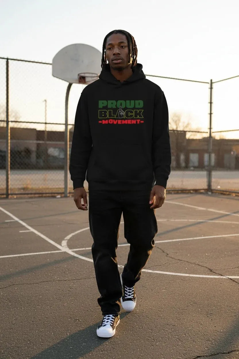 A man walking on an outdoor basketball court wearing a black hoodie with 'PROUD BLACK MOVEMENT' printed in green and red on the chest, paired with black sweatpants and white sneakers.
