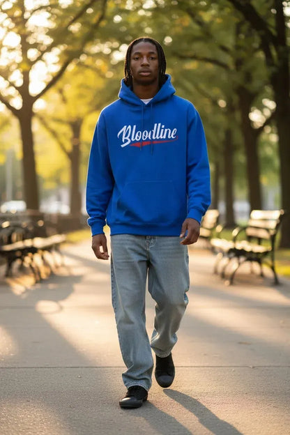 A man walking down a sunlit park path wearing a bright blue hoodie with 'Bloodline' printed across the chest in white script and a small red accent, paired with light gray jeans and black shoes.