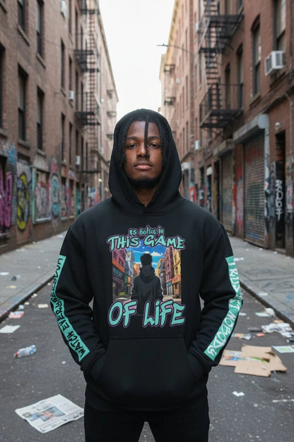 A man wearing a black pullover hoodie with a colorful graphic print on the chest and green text down the sleeves, standing in an urban alleyway.