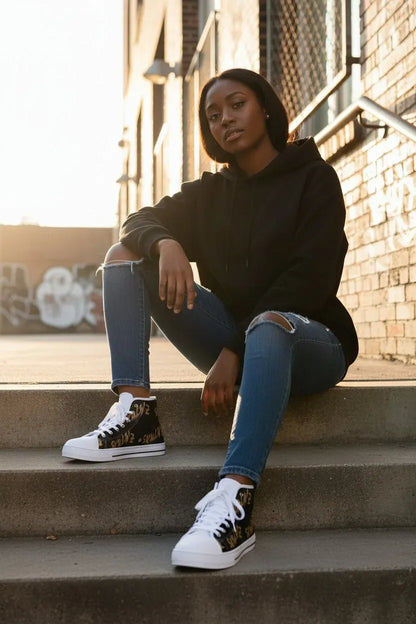 A woman sits on concrete steps outdoors against a brick wall, wearing a black hoodie, ripped blue jeans, and black high-top sneakers with white soles and laces.
