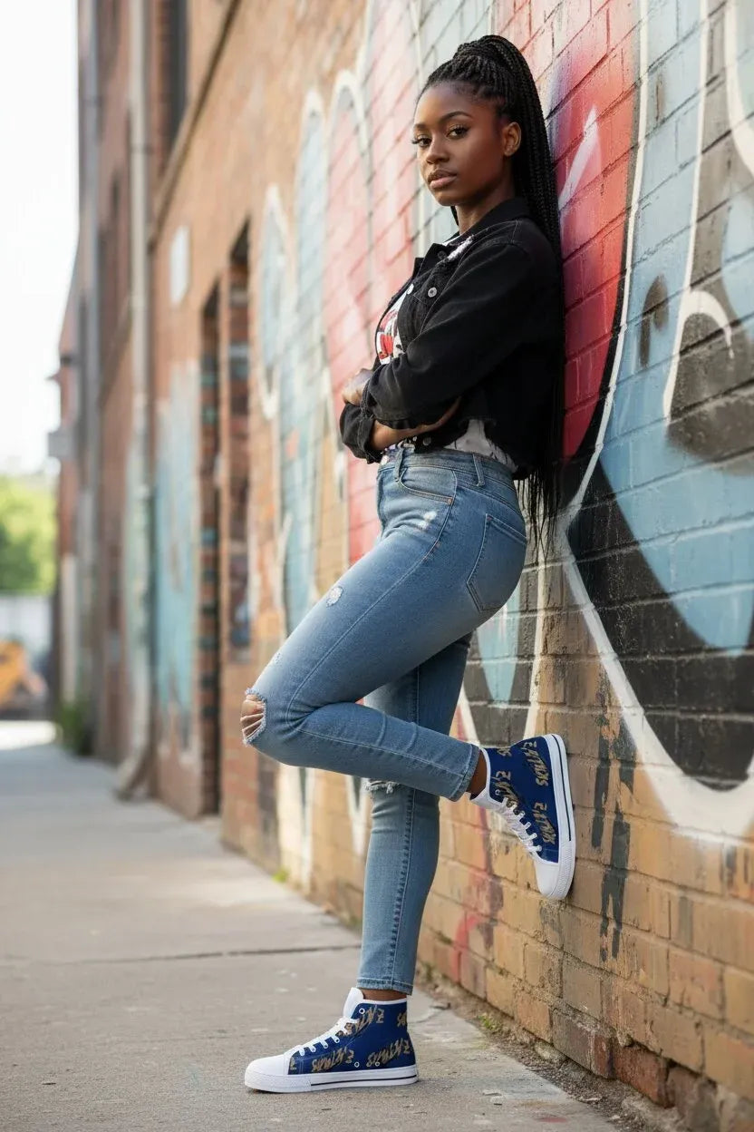 A woman posing in a city alleyway against a brick wall with graffiti, wearing light-wash blue skinny jeans, a black jacket, and blue high-top sneakers with gold lettering.