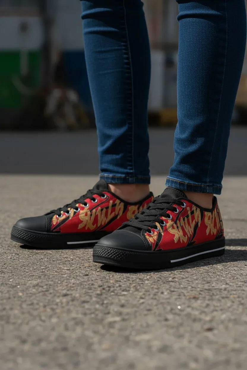 A person wearing red low-top sneakers with a yellow and orange flame graphic and black soles, paired with blue jeans, standing on a gray asphalt surface.